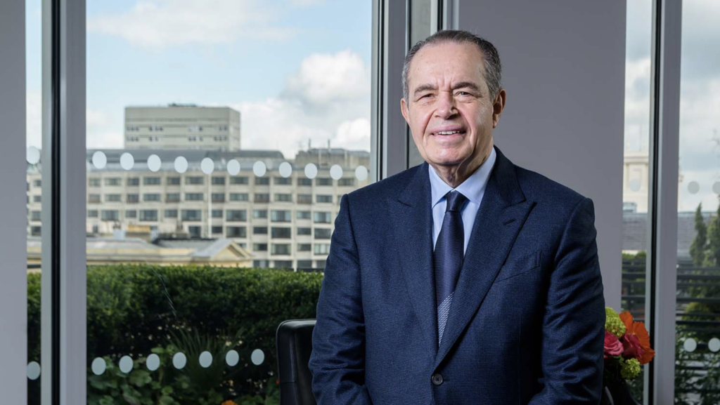 Sir Mohamed Mansour sits in front of a window overlooking a city skyline